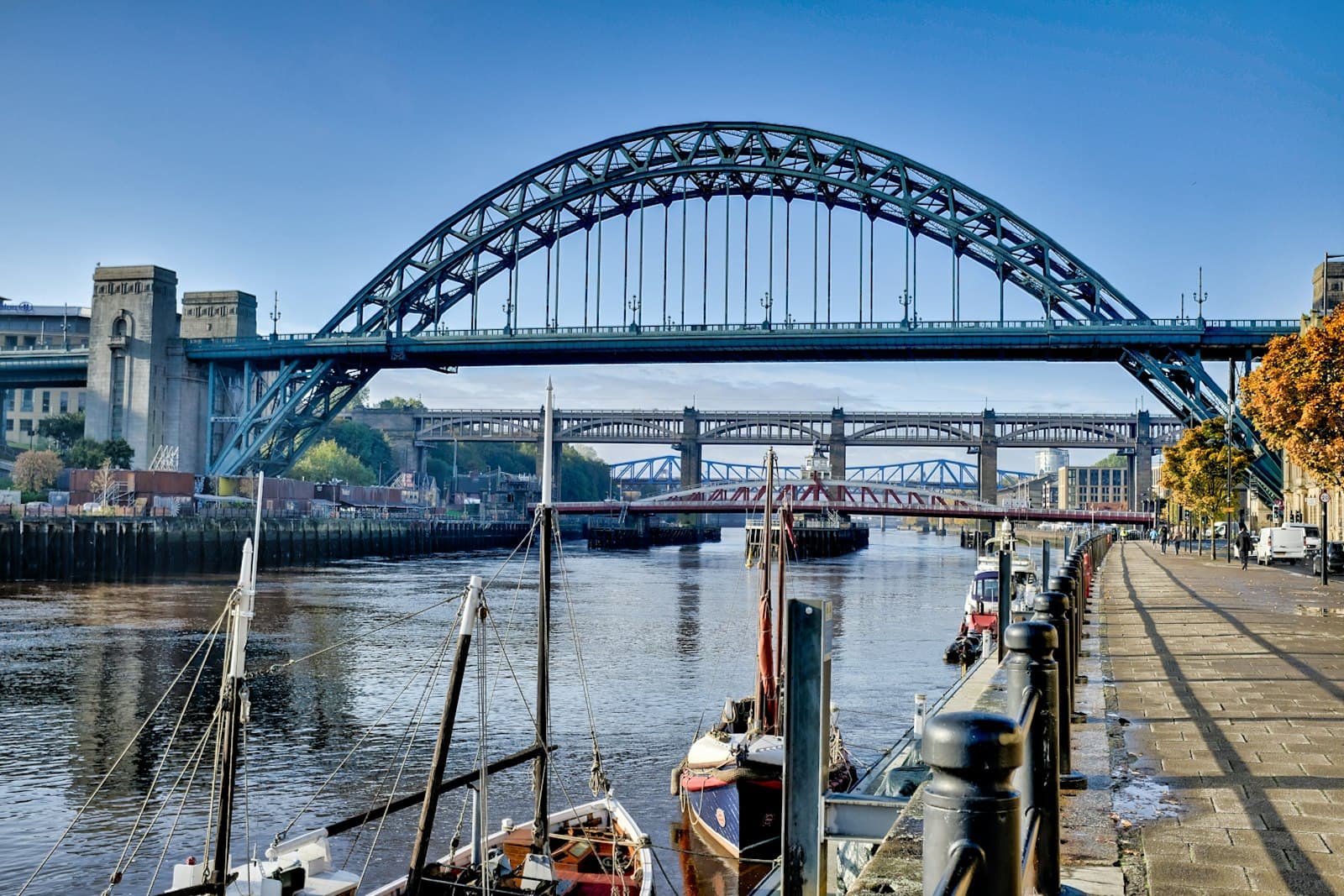 The Tyne Bridge arching over the River Tyne on a sunny autumn morning, with boats moored along the Newcastle Quayside