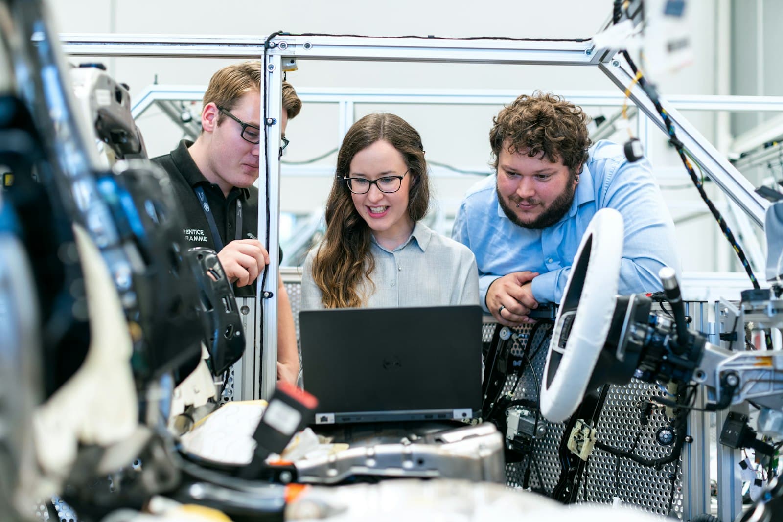 Three engineers gathered round a laptop in an automotive engineering workshop, working through a project together